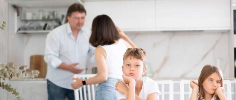 man and woman fighting while kids sit in foreground listening, looking upset
