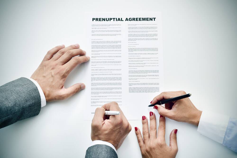 two sets of hands signing prenuptial agreement document seen from birds eye view