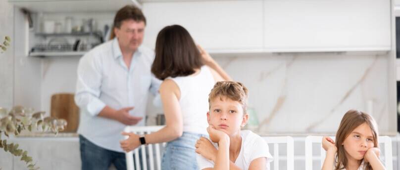 man and woman fighting while kids sit in foreground listening, looking upset